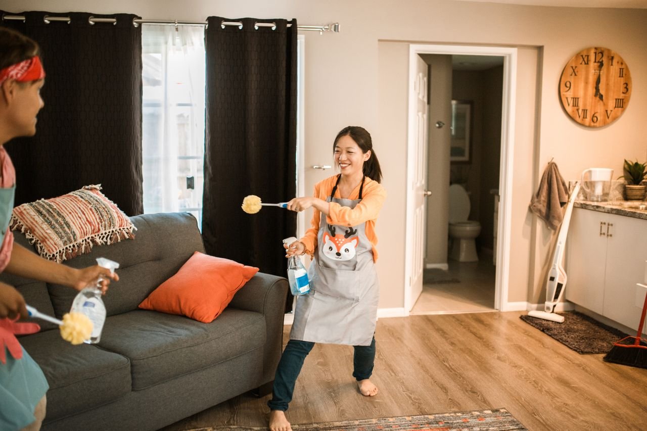 A cheerful couple engages in a playful cleaning session in their home.